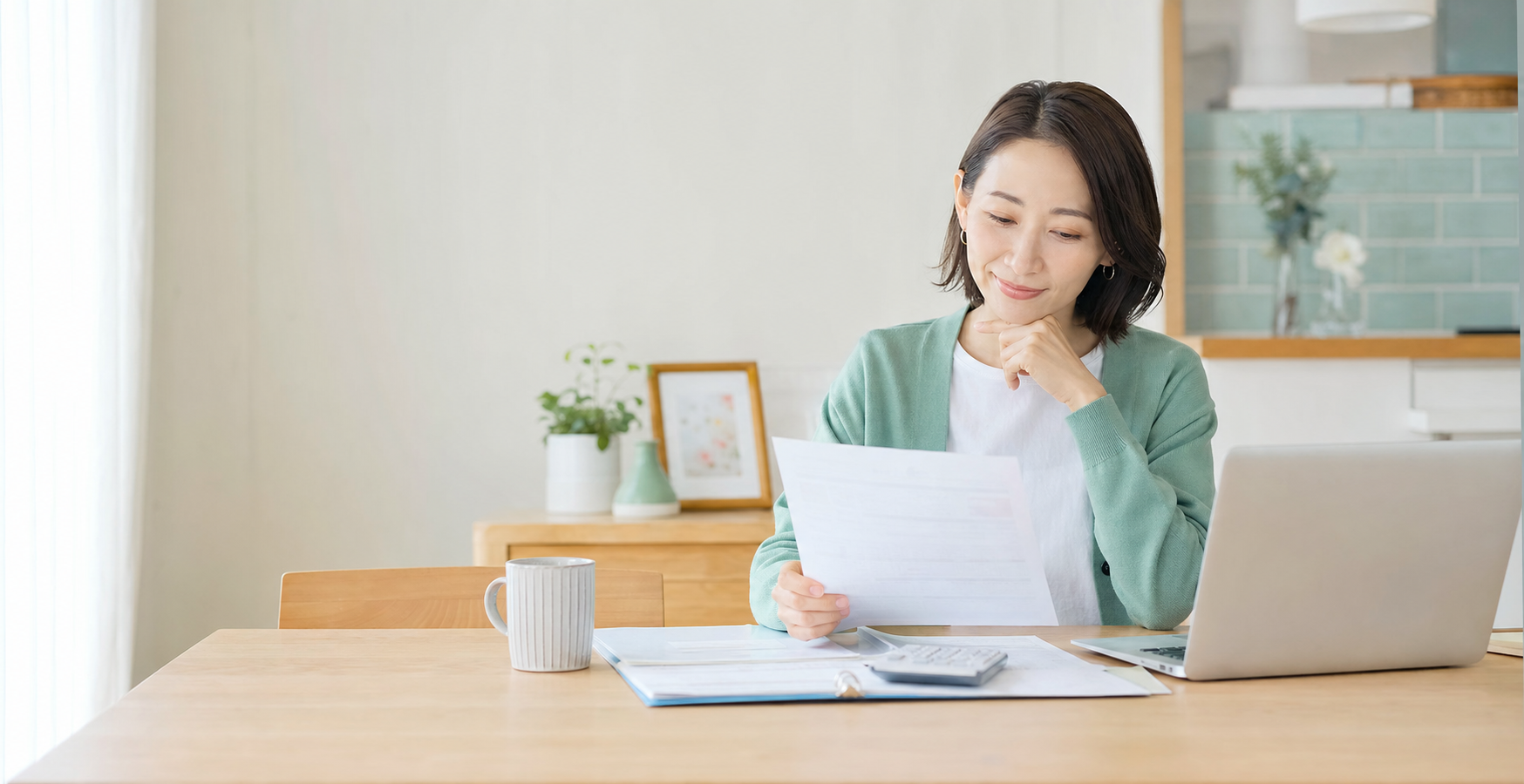 自宅でパソコンと書類を見ながら家計を確認する女性